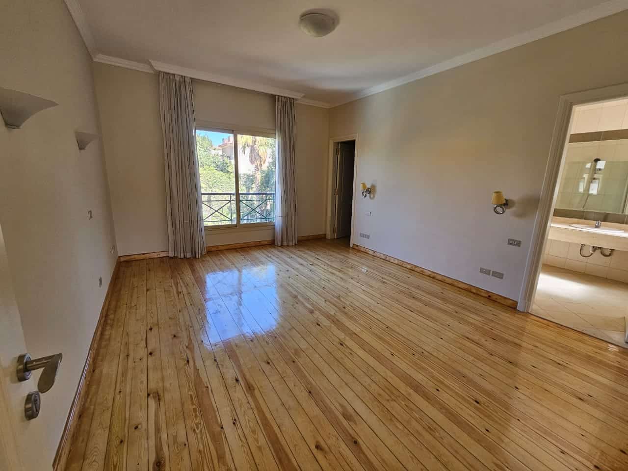 Spacious living room with large window, wooden floors, and nearby bathroom in Maadi Cairo apartment.
