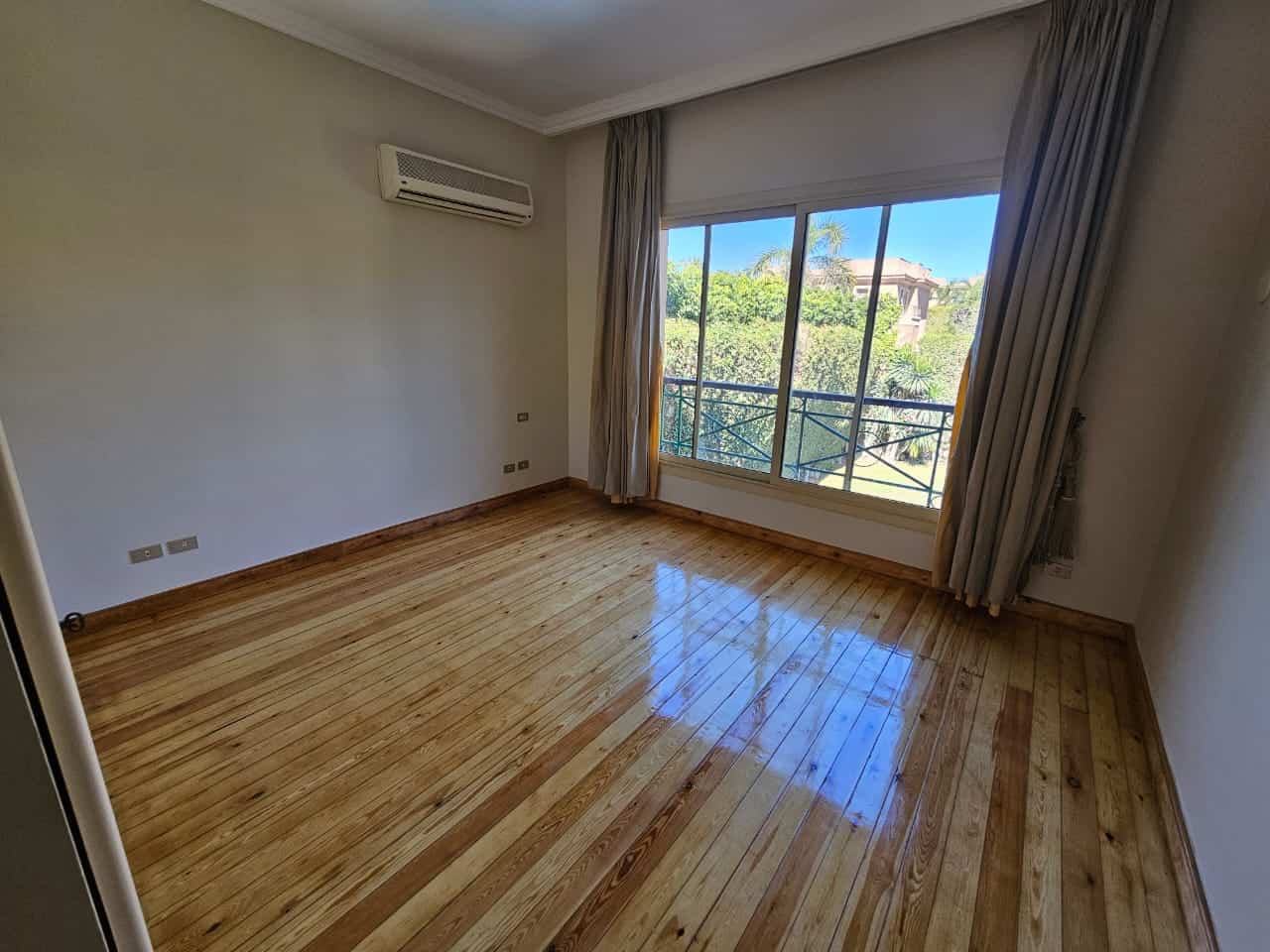 Bright living room with large window, balcony view, wooden floors, and natural sunlight.