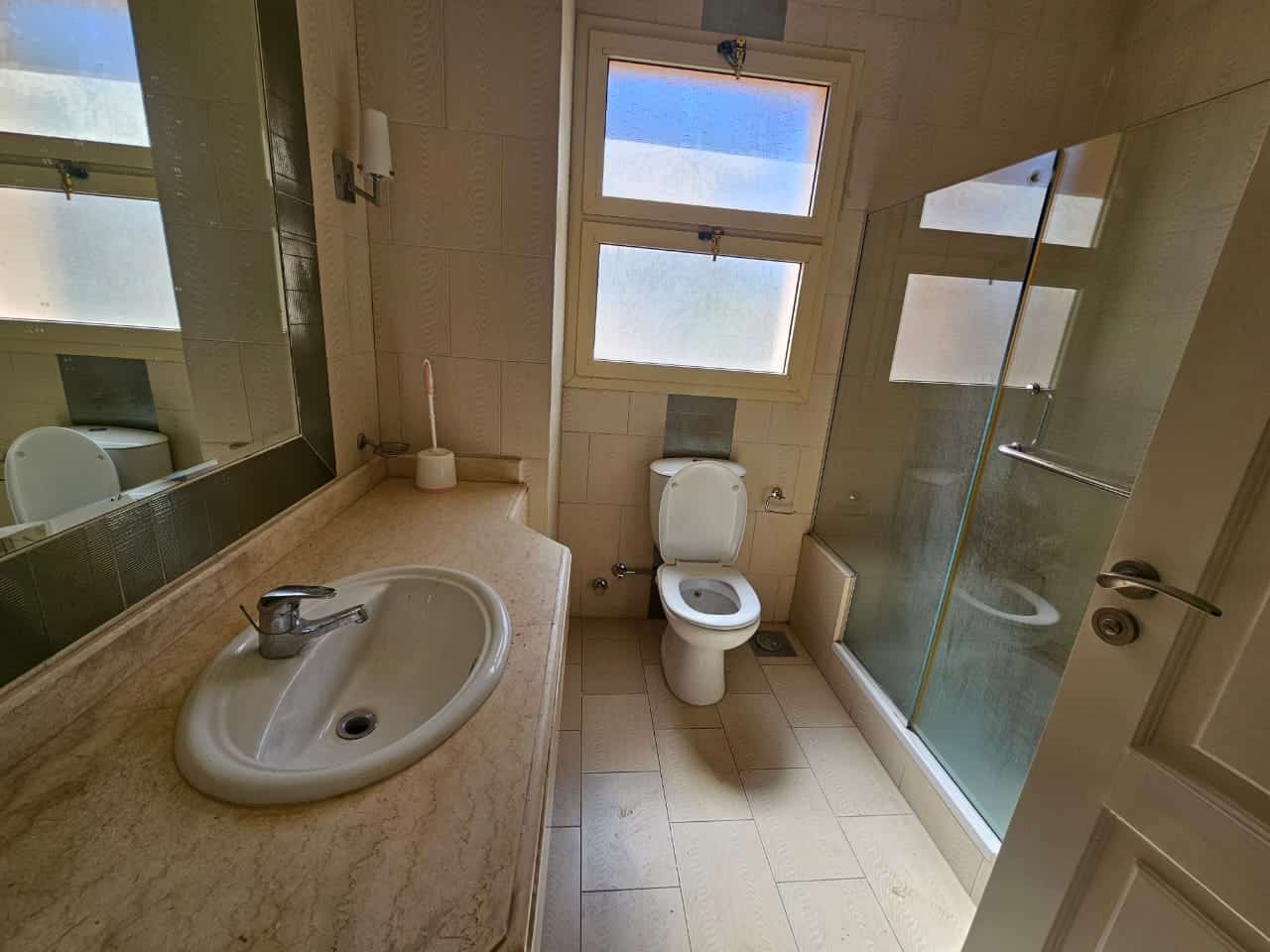 Bright bathroom with beige tiles, a large mirror, frosted windows, and a walk-in shower in Maadi Cairo apartments.