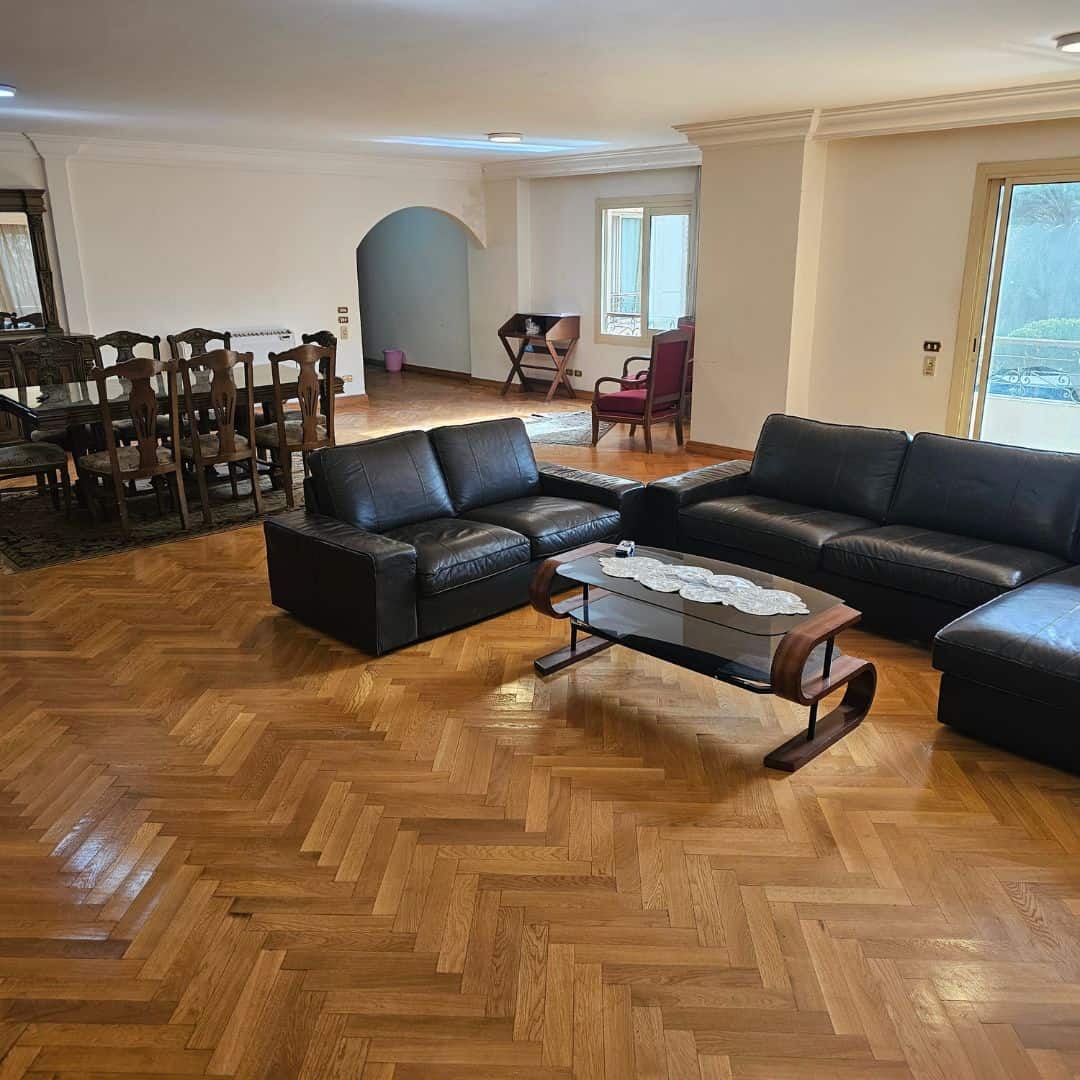 Bright living room with hardwood floors, black leather sofas, and ample natural light in Maadi Cairo.
