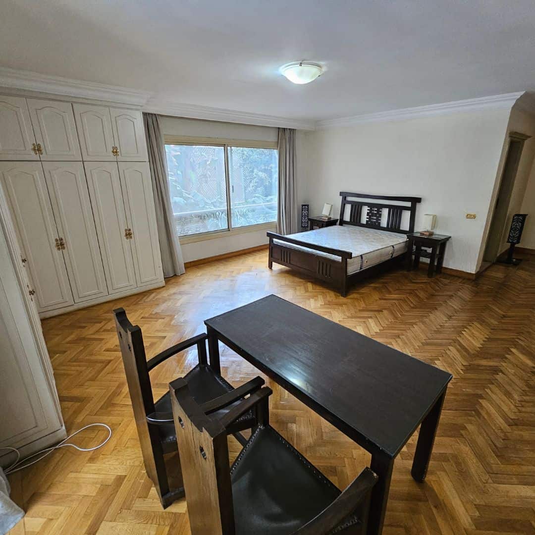 Spacious bedroom with wooden flooring, large window, and minimalist furniture in Maadi Cairo apartment.