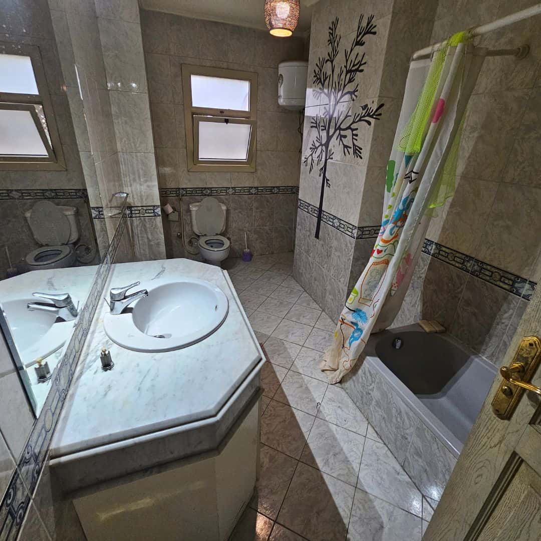 Bright bathroom with beige tiles, small bathtub, and window views in Maadi Cairo apartment.