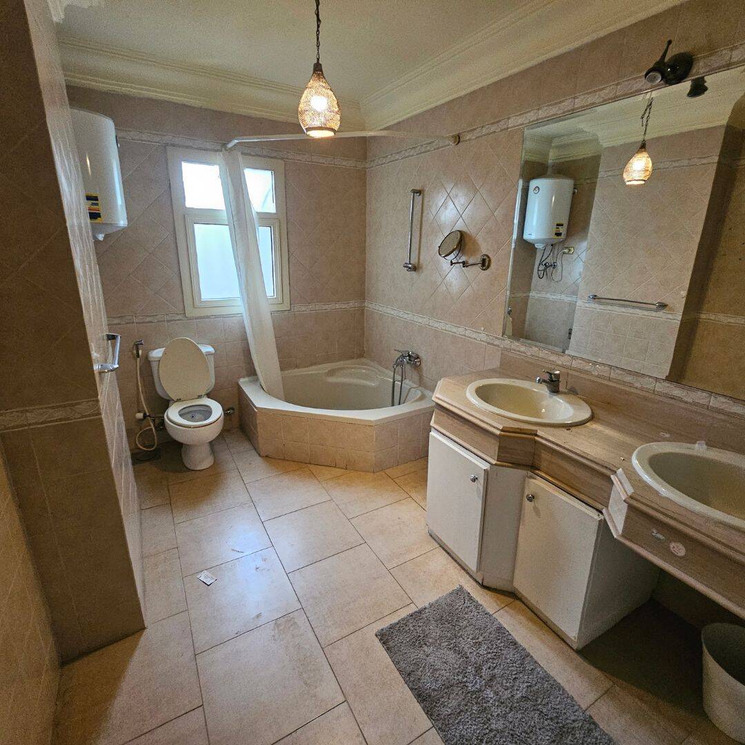 Spacious bathroom with double sinks, bathtub, toilet, and beige tiled walls in a Maadi Cairo apartment.
