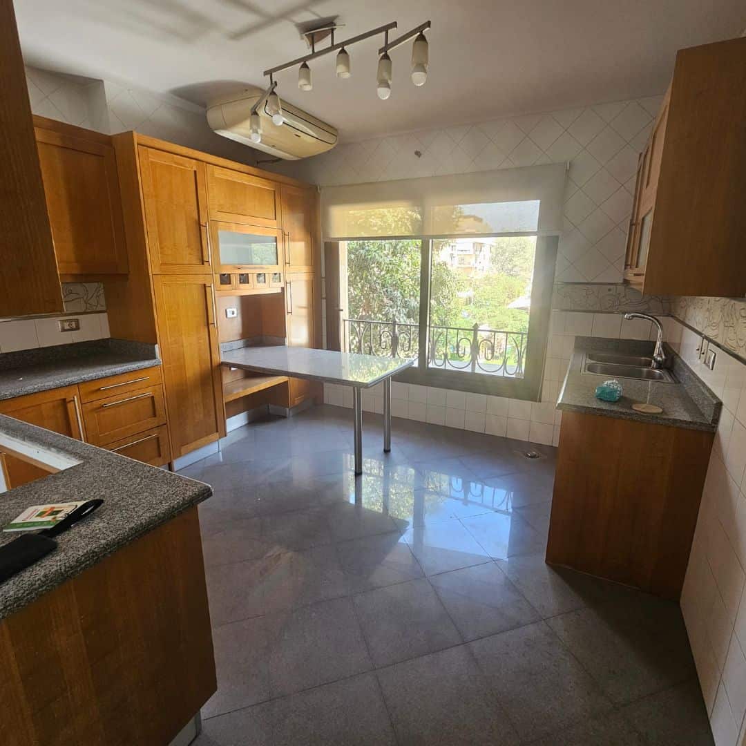 Bright airy kitchen with wooden cabinets and large window overlooking greenery in Maadi Cairo.