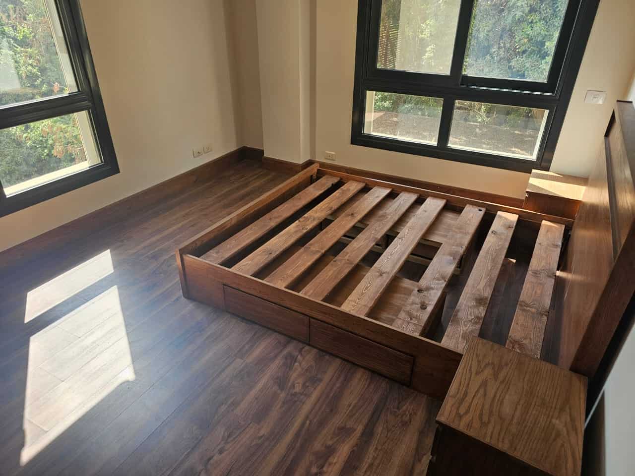Bright apartment bedroom with large windows, wooden flooring, and a bed frame ready for setup in Maadi Cairo.