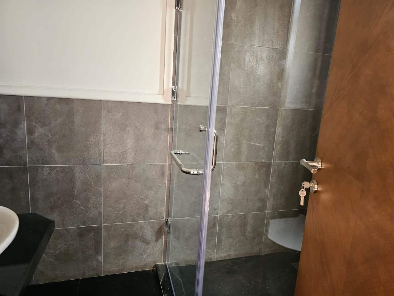 Modern bathroom with gray tiled walls and clear glass shower enclosure in Maadi Cairo.