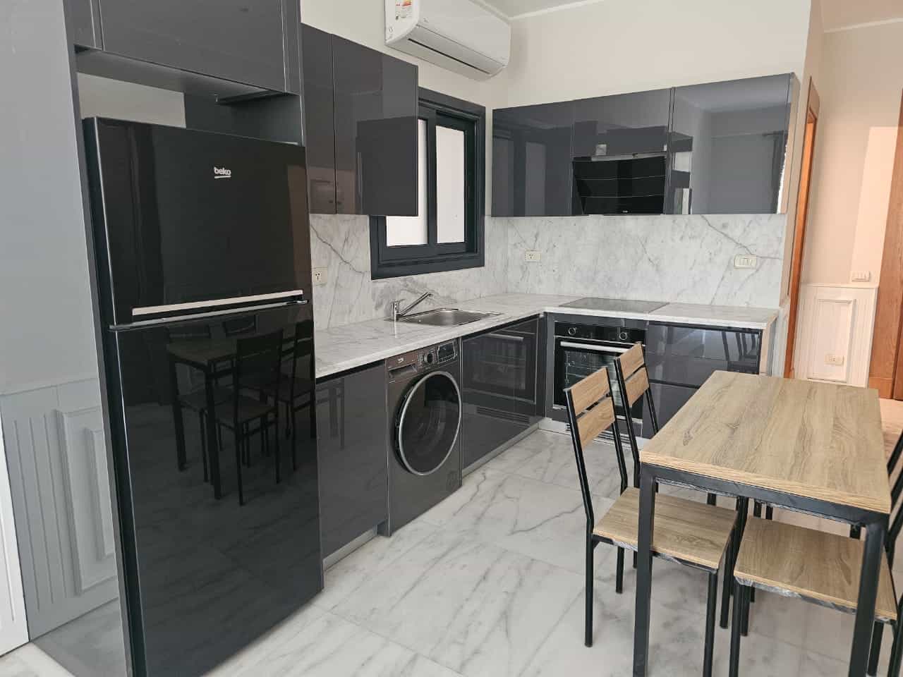 Modern gray kitchen with marble countertops, washing machine, and dining table in Maadi Cairo.