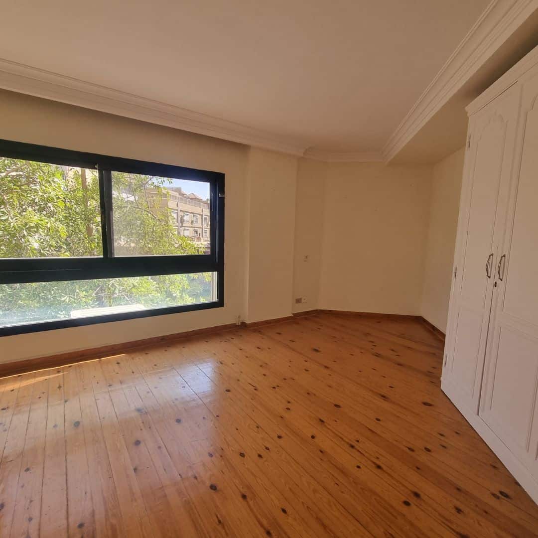 Spacious Duplex For Sale In Maadi Sarayat (7) Bright empty bedroom with large window and wooden flooring in Maadi Cairo Egypt.